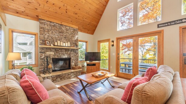 L’intérieur d’une cabane avec une cheminée en pierre, un plafond en bois et un balcon orné du feuillage automnal.