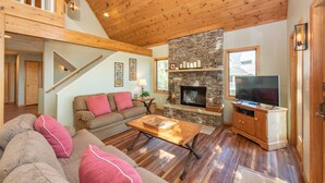 Un vaste salon doté d’une cheminée en pierre, d’un plafond en bois et d’un téléviseur posé sur un meuble en bois.