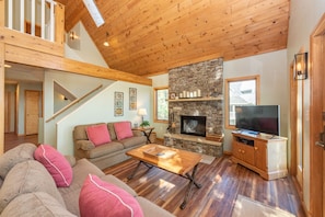 A spacious living room with a stone fireplace, wooden ceiling, and a television on a wooden cabinet. - Slopeside Luxury Dog Friendly Retreat w/ Hot Tub (McHenry)