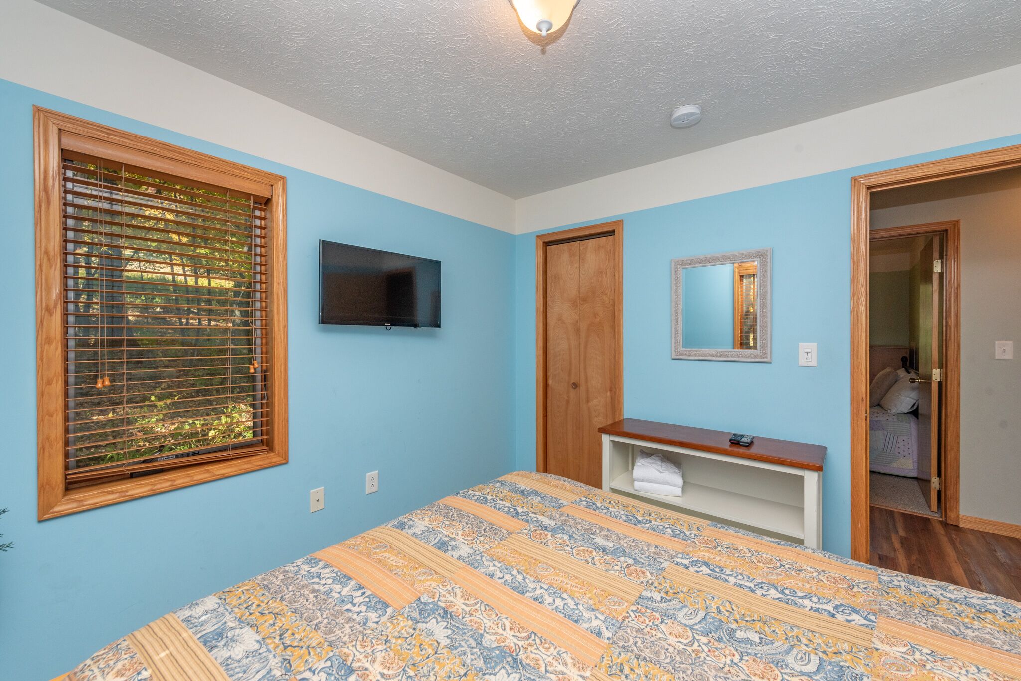 A bedroom with a bed, a TV mounted on the wall, a wooden door, and a mirror.