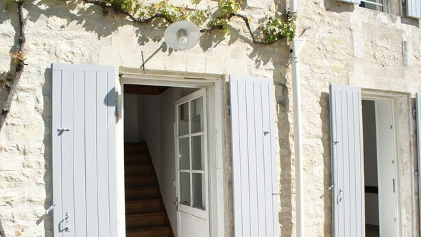 Un escalier menant à une pièce dotée de volets blancs et d’un mur en pierre.