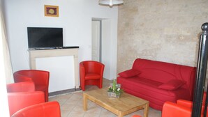Un salon avec un canapé rouge, deux fauteuils rouges, une table basse en bois et un téléviseur à écran plat fixé sur un meuble blanc.