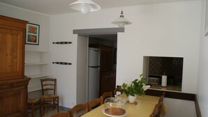 Un coin repas avec une table dressée pour quatre personnes, un buffet en bois et une cuisine visible à travers une porte ouverte.