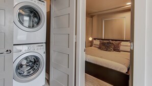 A hotel room with a washing machine, a bed with a headboard, and a bedside table. - Woodside Ave - Close to Sundance Locations - Private Hot Tub (Park City)