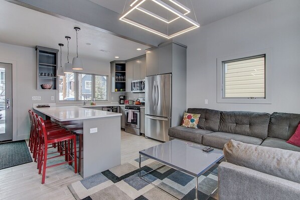 A modern kitchen with a central island, stainless steel appliances, and a grey sofa in a living area.