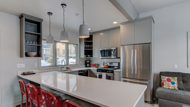 A modern kitchen with a large island, stainless steel appliances, and red bar stools. - Woodside Ave - Close to Sundance Locations - Private Hot Tub (Park City)