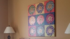A bedroom with a bed, a headboard, a wall with a floral artwork, a lamp, and a nightstand. - Vacation Rental Available (Scottsdale)