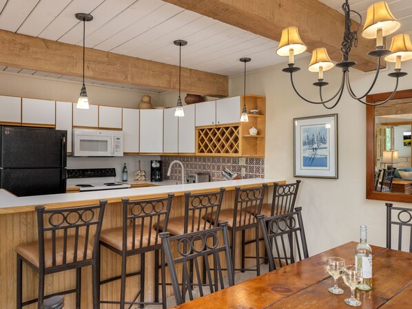 Una cocina moderna con armarios blancos, un refrigerador negro y una isla de madera con taburetes de bar.