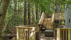 Eine Holzterrasse mit Korbmöbeln, einer Treppe und Blick ins Waldgebiet.
