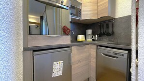 A compact kitchen with a refrigerator, microwave, coffee maker, and dishwasher. - Cozy 4-Person Apartment, Ski-In/Ski-Out, West-Facing Balcony, Les Menuires (Les Menuires)