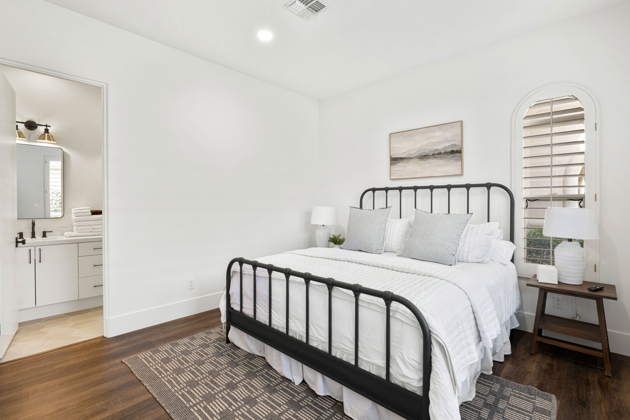 A bedroom with a bed, bedside table, lamp, and a window with blinds.