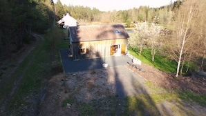 A rustic wooden building with a sloped roof, a large open porch, and a paved driveway. - Small house in the middle of the forest.  (Saint-Remy)