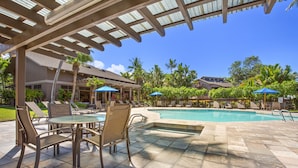 Un espace piscine aménagé avec des chaises longues, une table et des parasols.