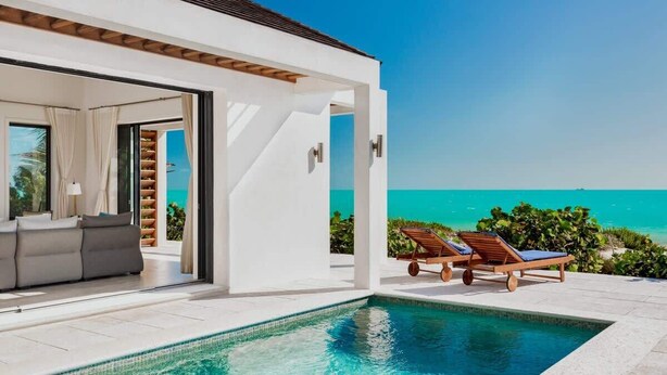 A modern poolside area with a clear view of the ocean, a white exterior, and a built-in seating area. - Brise De Mer 6 BR Villa (Long Bay)