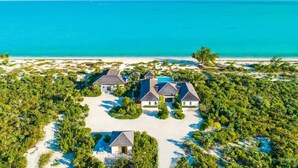 An aerial view of a coastal property with multiple houses, a beach, and a clear view of the ocean. - Brise De Mer 6 BR Villa (Long Bay)