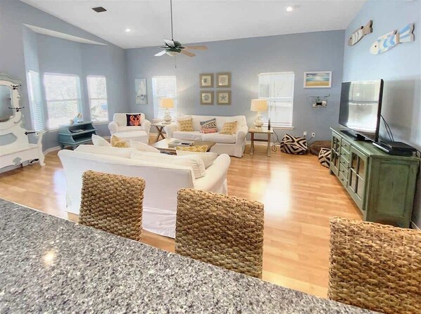 A living room with a white sofa set, a coffee table, and a TV. There are wicker chairs, a green cabinet, and a ceiling fan. - Private Pool-4 Bikes-Updated Home-`Endless Summer` (Santa Rosa Beach)