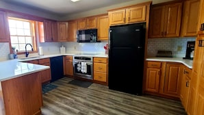 A kitchen with wooden cabinets, a black refrigerator, a microwave, and a sink. - Beautiful Lakefront w Private Beach/Hot Tub/ Boats/ Fire Pit (Long Pond)