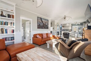 A spacious living area with a sofa, a coffee table, and a wicker chair. There are bookshelves filled with books and a painting on the wall.