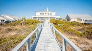 A coastal building with a wooden walkway leading to it, surrounded by dry vegetation. - Fairwinds: Inviting Oceanfront Home Built to Entertain (Caswell Beach)