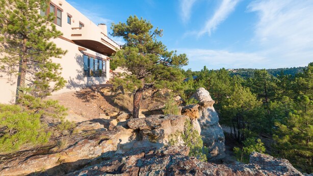 A modern building with a large glass window, surrounded by rocky terrain and pine trees. - Hidden Gem: Heated Pool, Gorgeous Mountain Views, 2.4 Acres inside City, A/C, EV (Colorado Springs)
