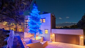 A modern house with a well-lit exterior, a staircase leading to the entrance, and a view of distant mountains. - Hidden Gem: Heated Pool, Gorgeous Mountain Views, 2.4 Acres inside City, A/C, EV (Colorado Springs)
