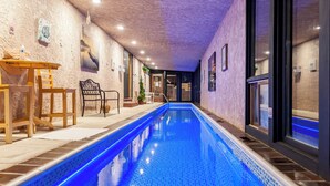 An indoor swimming pool with a blue tiled floor, wooden chairs, a small table with a bottle, and framed pictures on the walls. - Hidden Gem: Heated Pool, Gorgeous Mountain Views, 2.4 Acres inside City, A/C, EV (Colorado Springs)