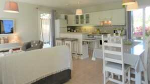 A modern kitchen with white cabinets, a dining area with white chairs, and pendant lights.
