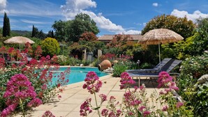 A pool area with lounge chairs and umbrellas, surrounded by vibrant flowers and greenery.