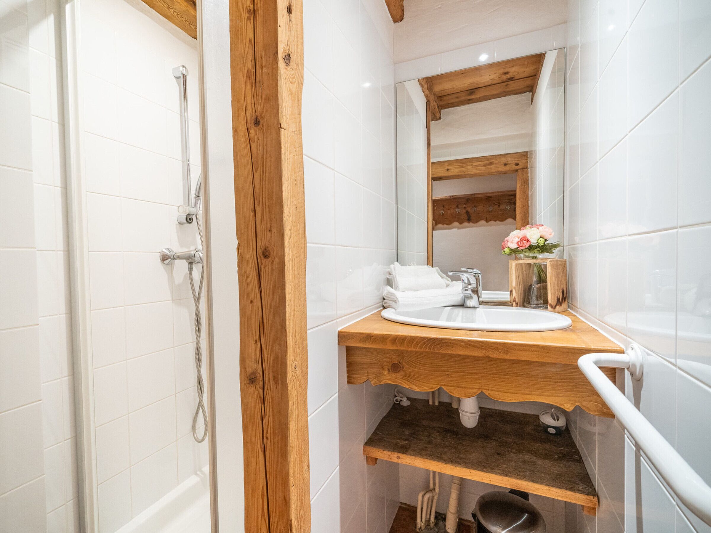 A bathroom with white tiles, a wooden vanity, a sink, a mirror, and a shower.