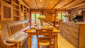 A wooden cabin interior with a dining table set for four, a bench with cushions, and a television on a wooden stand.