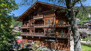 A traditional wooden chalet with multiple balconies, a stone foundation, and a surrounding garden.