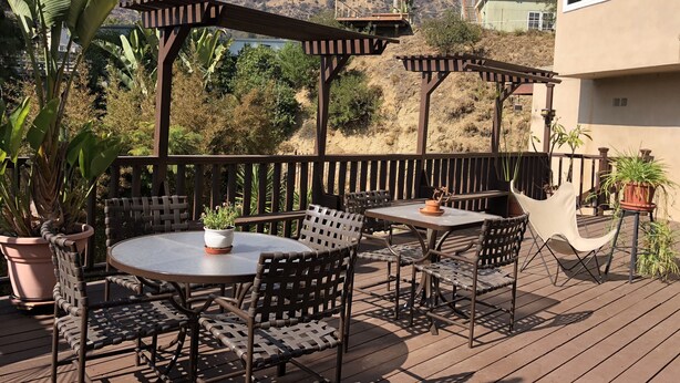 Eine Terrasse im Freien mit Tisch und Stühlen, umgeben von Blumentöpfen und einer Pergola.