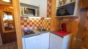 Una cocina compacta con microondas, lavamanos y una cafetera roja.