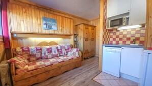 Una habitación acogedora con un sofá de madera, un armario de madera y una cocina equipada con microondas y lavavajillas.