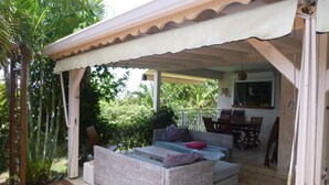 A covered outdoor seating area with a wicker sofa and a dining table. - Villa for 6 people, swimming pool, sea view, close to Sainte Anne beaches (SAINTE ANNE)