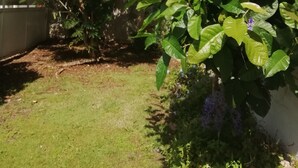 A garden with various plants and flowers, a lawn, and a blue building in the background. - Villa for 6 people, swimming pool, sea view, close to Sainte Anne beaches (SAINTE ANNE)
