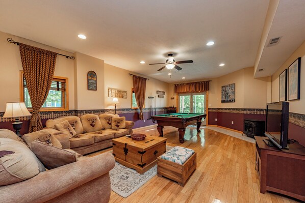 A spacious living room with a pool table, a sofa set, a wooden coffee table, and a television.