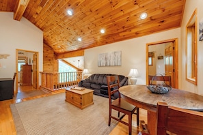 A spacious living area with a wooden ceiling, a dining table with chairs, a sofa, and a staircase leading to an upper level.