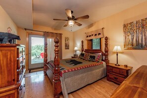 A bedroom with a wooden bed, a ceiling fan, a nightstand with a lamp, a dresser, and a painting on the wall.