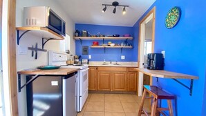 A compact kitchen with a refrigerator, microwave, stove, and wooden cabinets. There are shelves above the counter holding various kitchen items.