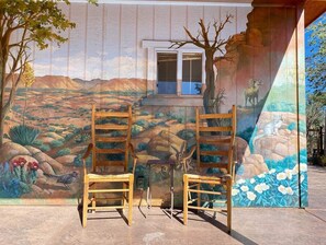 Two wooden chairs in front of a mural with a window above them.
