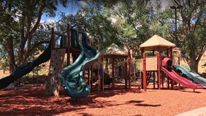 A playground with slides and climbing structures, surrounded by trees.