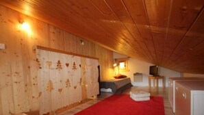 A cozy attic bedroom with wooden walls, a red carpet, a bed, a TV, and a small cabinet. - Cozy apartment for 5, south balcony, near slopes (Les Saisies)