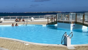 A swimming pool with a view of the ocean, a lifeguard station, and a covered area with chairs. - Deluxe Studio on Orient Bay (saint martin)