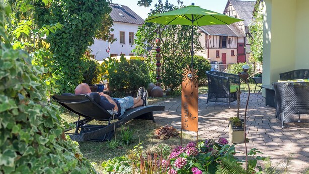 Un patio con una silla de descanso, una sombrilla verde y plantas en macetas.
