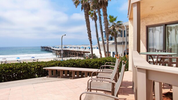 Un patio frente a la playa con sillas de descanso, vista al océano y un muelle al fondo.