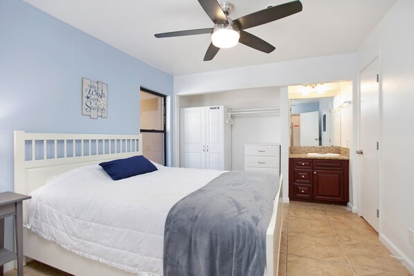 Une chambre à coucher comprenant un lit, un ventilateur de plafond, une commode et une salle de bain avec un lavabo et un miroir.