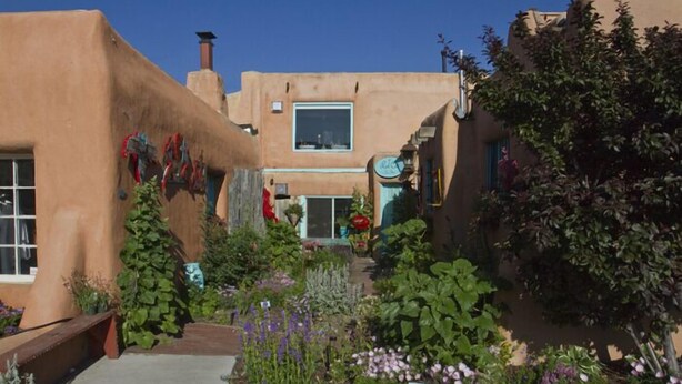 Un edificio tradizionale in adobe con un giardino antistante, che include diverse piante e fiori.