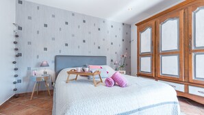 A neatly arranged bedroom with a large bed, a wooden wardrobe, and a bedside table with a lamp.