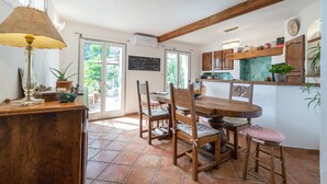 A kitchen with wooden furniture, a dining table, and chairs. There is a window with a view of greenery outside.